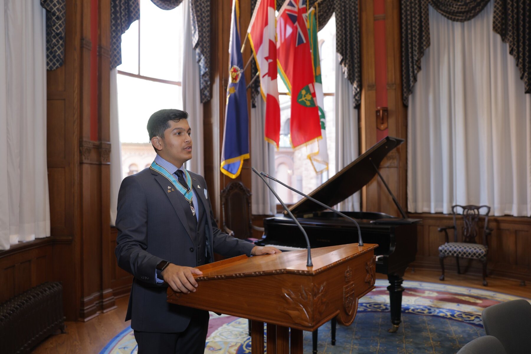 Adil Mukhi speaking at the podium at Queen's Park